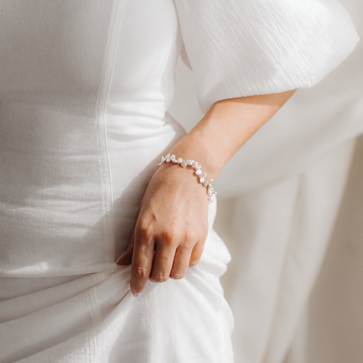 Close-up of a wrist wearing a gold-plated sterling silver Keshi pearl bracelet, styled with a white dress in soft natural light.