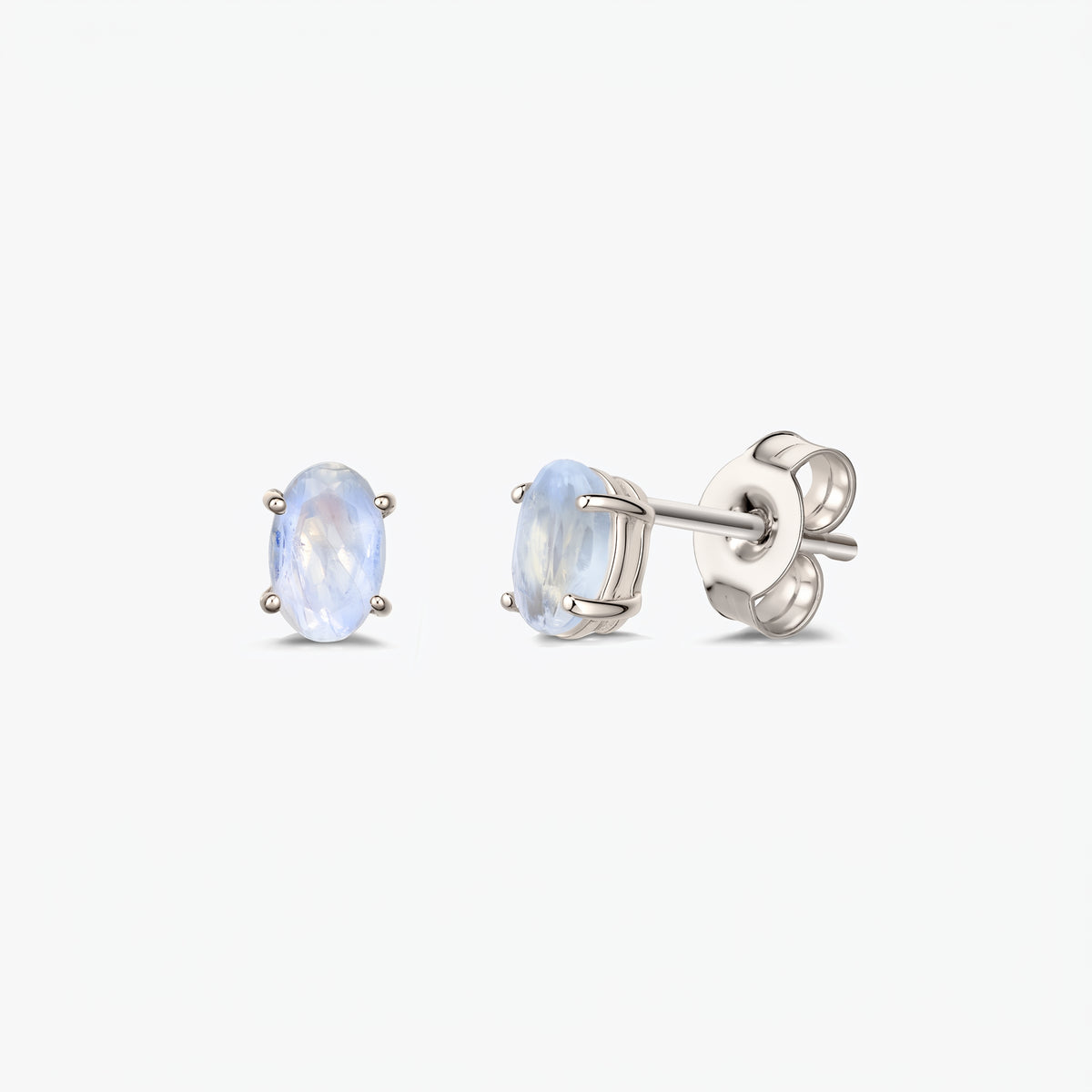 Pair of silver moonstone stud earrings with oval faceted stones in four-prong settings and butterfly push backs, displayed on a white background.