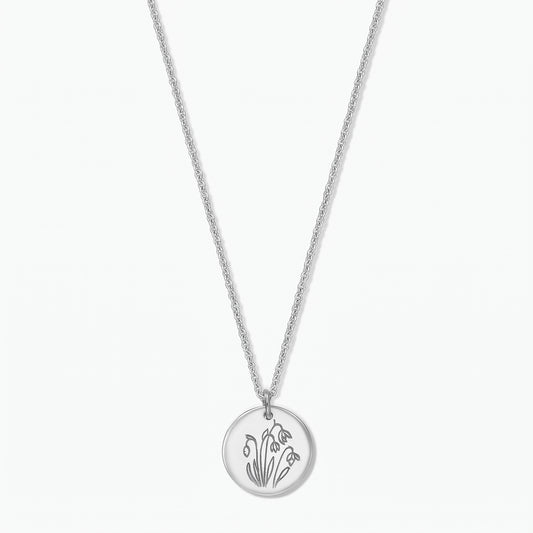 Sterling silver birth flower necklace with a round disc pendant engraved with January snowdrops on a fine chain, isolated on a white background.