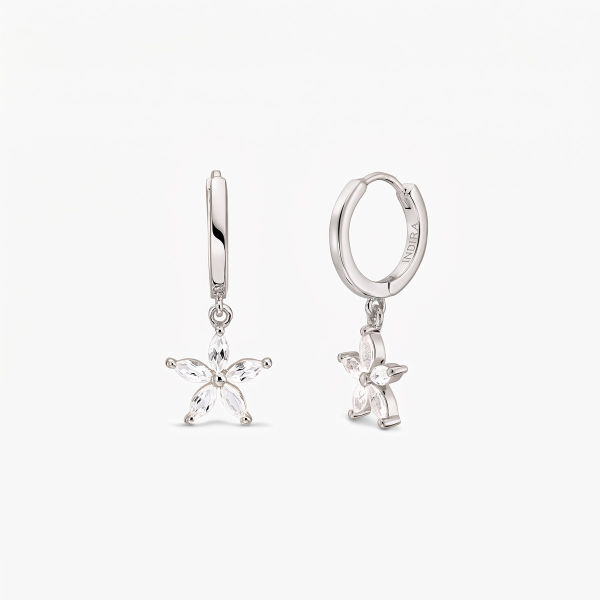 Pair of sterling silver huggie hoop earrings with dangling five-petal blossom charms set with white topaz on a white background.