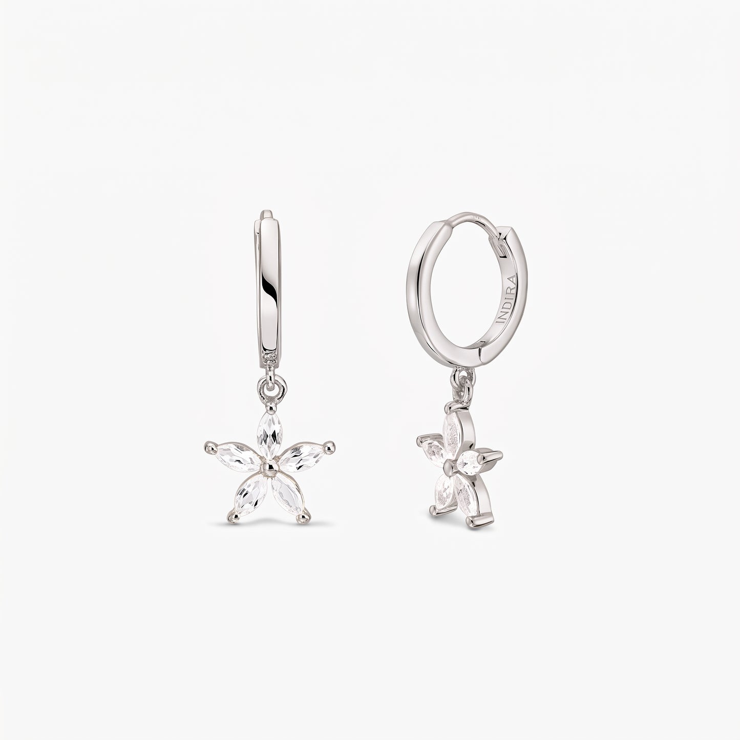 Pair of sterling silver huggie hoop earrings with dangling five-petal blossom charms set with white topaz on a white background.