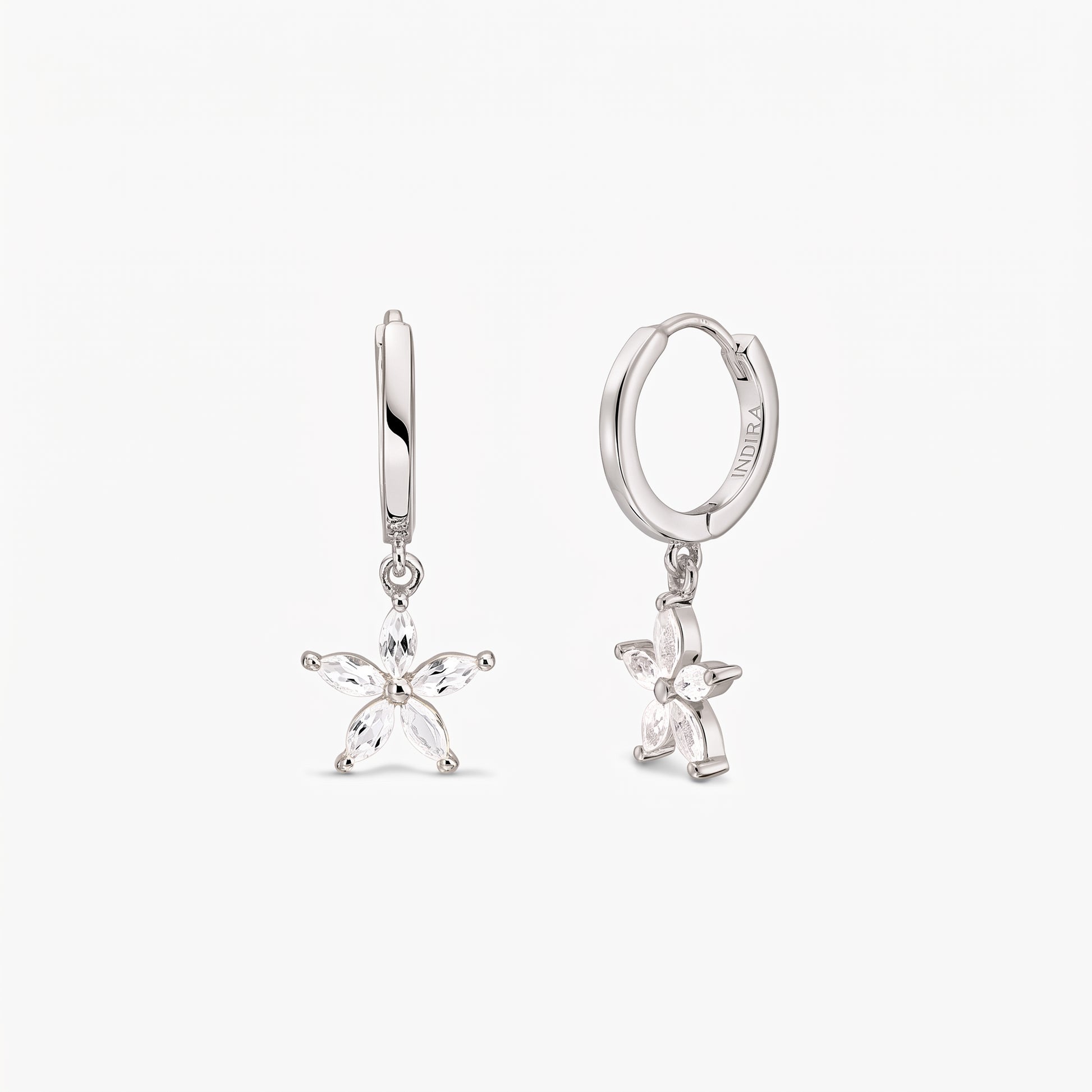 Pair of sterling silver huggie hoop earrings with dangling five-petal blossom charms set with white topaz on a white background.