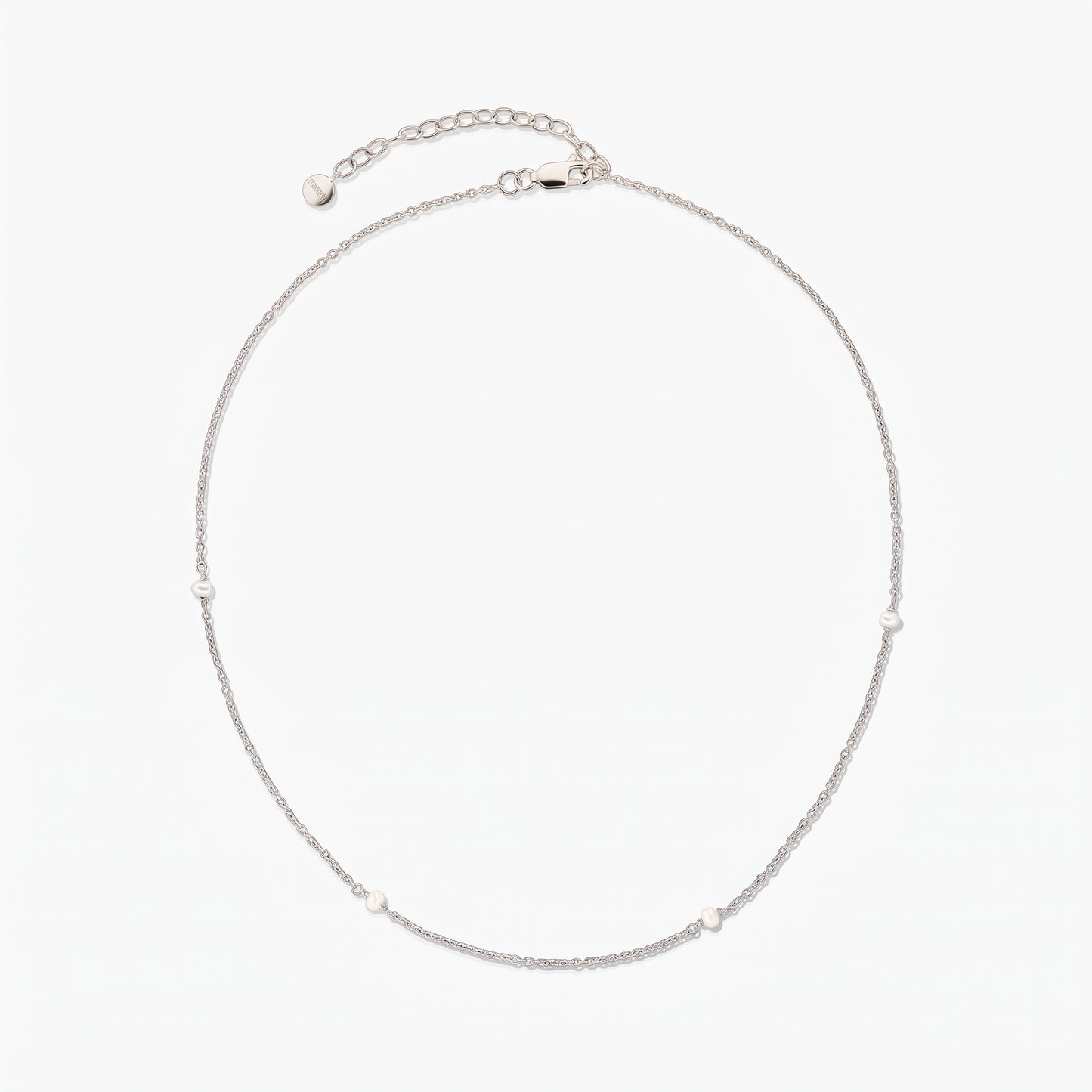 Delicate silver chain necklace with tiny white pearl stations, arranged in a circle on a white background, featuring an adjustable extender and lobster clasp.