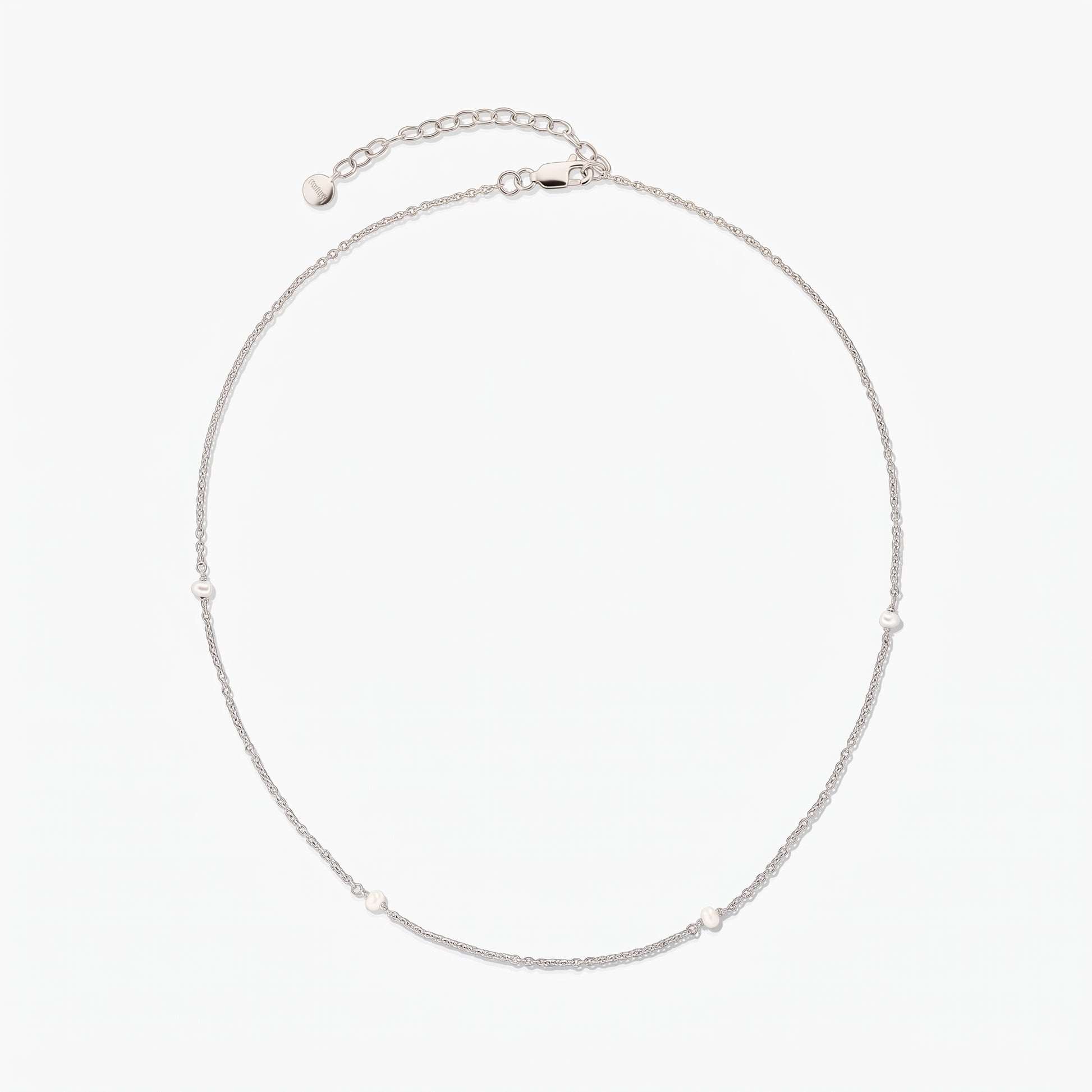 Delicate silver chain necklace with tiny white pearl stations, arranged in a circle on a white background, featuring an adjustable extender and lobster clasp.